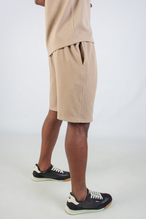 Person wearing beige shorts and black sneakers on a white background